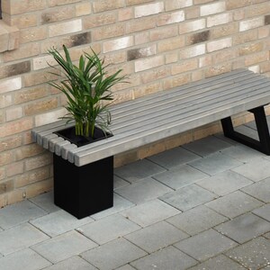 May include: A gray wooden bench with black metal legs and a built-in planter box. A green plant is growing in the planter box.