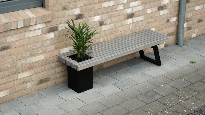 May include: A gray wooden bench with black metal legs and a built-in planter box. A green plant is growing in the planter box.