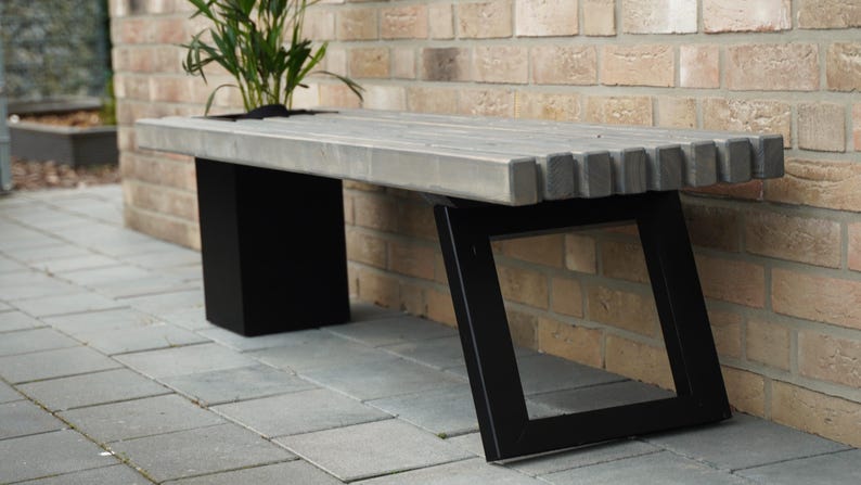 May include: A concrete bench with a gray top and black metal legs. The bench has a unique design with a zig-zag pattern on the underside of the top.