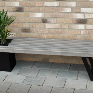 May include: A gray wooden bench with black metal legs and a built-in planter. The planter is filled with a green plant.