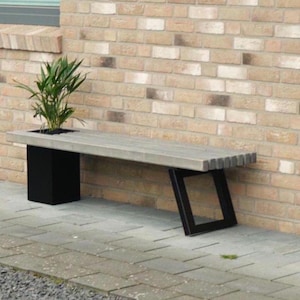 May include: A gray wooden bench with black metal legs and a built-in planter. The bench is placed against a brick wall and has a small plant growing in the planter.