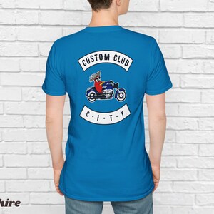 May include: A blue t-shirt with a white patch on the back that says "CUSTOM CLUB CITY" with a cartoon of a person riding a motorcycle.