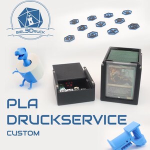 Könnte beinhalten: Das Bild zeigt einen blau-weißen Toilettenpapierhalter in Dinosaurierform, eine schwarze Box mit Würfeln und einen schwarzen Kartenhalter mit grünen Karten. Außerdem sind blaue Token und der Text "PLA DRUCKSERVICE CUSTOM" zu sehen.
