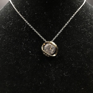 May include: A silver chain necklace with a gold-colored pendant. The pendant features a large, clear, round stone encircled by a gold-colored metal setting. Small, clear stones are set into the gold setting.