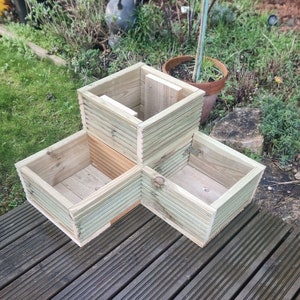 May include: A three-tiered wooden planter with three square compartments. The planter is made of unfinished wood and is sitting on a wooden deck.