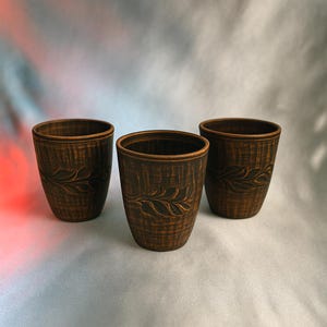 Könnte beinhalten: Drei braune Keramikbecher mit einem Blattdesign. Die Becher stehen auf einer hellgrauen Oberfläche.