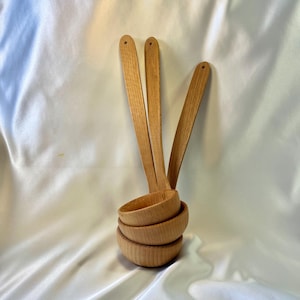 May include: A set of four wooden ladles with long handles and rounded bowls. The ladles are made of light-colored wood and have a smooth finish. The bowls are stacked together, and the handles are fanned out.