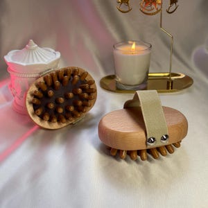 Op de afbeelding: Twee houten lichaamsborstels met natuurlijke borstels. Eén borstel heeft een beige stoffen band. Beide borstels zijn ovaalvormig en hebben een lichtbruine kleur.