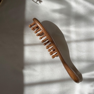 Puede incluir: Un peine de madera para el cabello con un mango curvo y dientes redondeados. El peine es de madera marr&oacute;n oscuro y tiene un acabado liso. Dise&ntilde;ado para masajes del cuero cabelludo y cuidado del cabello.