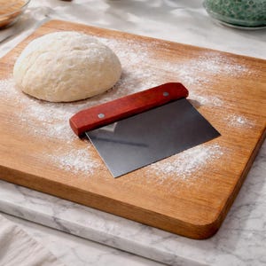 May include: A handmade, wooden cutting board with a natural finish. The rectangular board features a juice groove and a handle. Dimensions are approximately 18 inches long, 12 inches wide, and 1 inch thick.