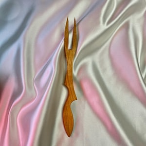 May include: A wooden fork with a unique, curved design. The fork is made of light brown wood and has two prongs.