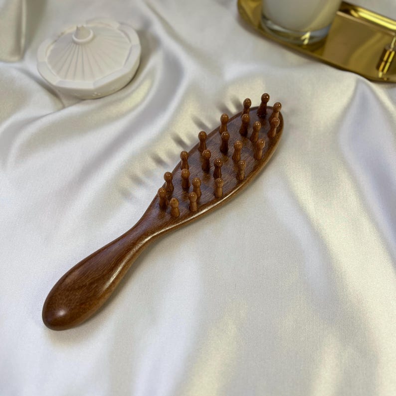 Puede incluir: Un cepillo de pelo de madera de color marr&oacute;n oscuro. El cepillo tiene un mango largo y ovalado y una cabeza con cerdas de madera redondeadas y espaciadas uniformemente. Dise&ntilde;ado para el cuidado y el peinado del cabello.