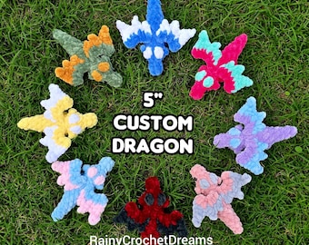 May include: Eight small, 12.7 cm custom crochet dragon plushies arranged in a circle. The dragons feature various colour combinations including blue and white, pink and teal, purple and light blue, peach and pink, red and black, yellow and white, and green and orange. The text 5" CUSTOM DRAGON and RainyCrochetDreams is visible.