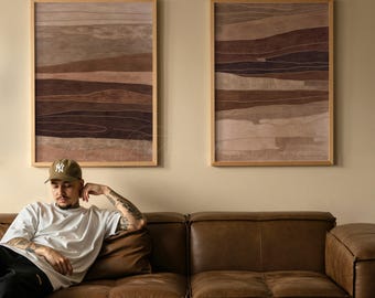 May include: Two rectangular wall art prints in light wood frames featuring abstract horizontal layers in shades of brown, beige, and dark chocolate. The artwork displays organic, flowing lines that mimic geological strata or landscape horizons.