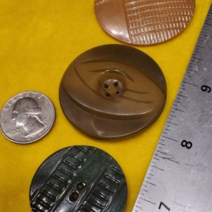 Puede incluir: Tres botones vintage con diferentes diseños y colores. Los botones son redondos y tienen un agujero en el centro. El primer botón es marrón con un patrón geométrico. El segundo botón es marrón con un patrón ondulado. El tercer botón es verde con un patrón rayado.