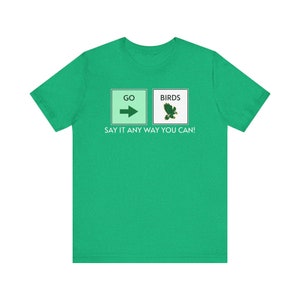 May include: A green t-shirt with a white graphic of two signs. The left sign says "GO" with an arrow pointing to the right. The right sign says "BIRDS" with a green bird graphic. The text below the signs says "SAY IT ANY WAY YOU CAN!"