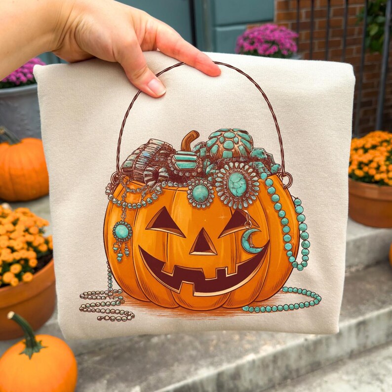 May include: A beige tote bag featuring a smiling orange jack-o'-lantern design. The pumpkin is adorned with turquoise-colored jewelry and a crescent moon. A brown handle arches over the top of the bag.