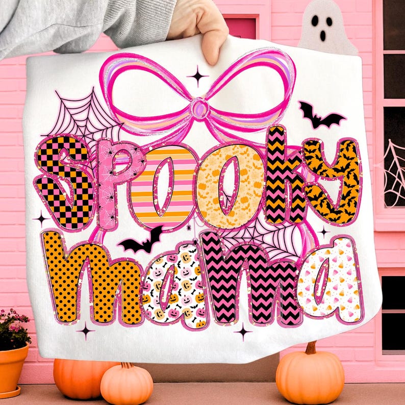 Peut inclure: Une couverture blanche sur le th&egrave;me d'Halloween avec l'inscription "Spooky Mama" dans un design color&eacute;. Le motif comprend des &eacute;l&eacute;ments roses, oranges et noirs, tels que des toiles d'araign&eacute;es, des chauves-souris et des citrouilles. Un grand n&oelig;ud rose est en haut.