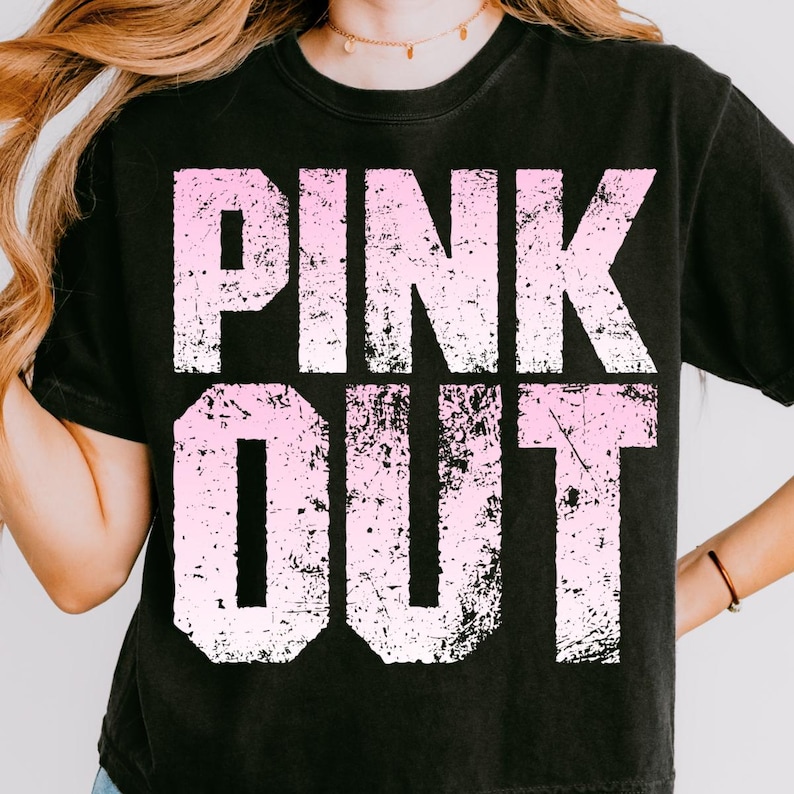 Puede incluir: Camiseta negra con las palabras "PINK OUT" en letras blancas y rosas desgastadas. La camiseta tiene cuello redondo y mangas cortas. El texto est&aacute; en negrita y en bloque.