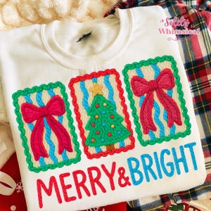 May include: White sweatshirt with embroidered Christmas designs. Features three rectangular patches with a red bow, a green Christmas tree, and another red bow. The words "MERRY & BRIGHT" are embroidered in red and blue.