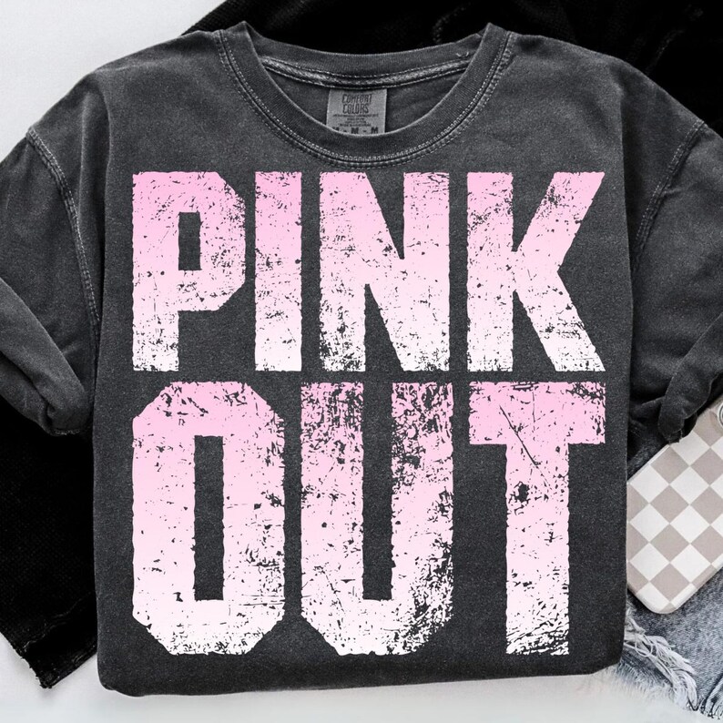 Puede incluir: Una sudadera gris oscuro con las palabras "PINK OUT" en letras blancas grandes y desgastadas con un degradado rosa. La sudadera tiene cuello redondo y mangas largas. El texto est&aacute; centrado en la parte delantera.