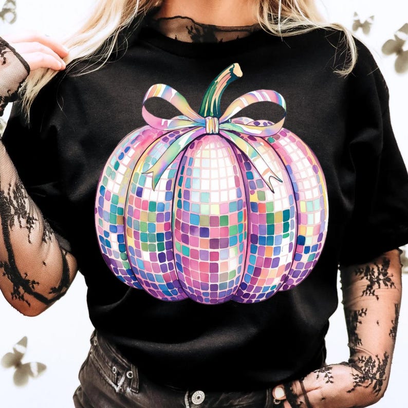 Puede incluir: Camiseta negra con un dise&ntilde;o de calabaza de bola de discoteca colorida. La calabaza est&aacute; hecha de peque&ntilde;os azulejos cuadrados en tonos de rosa, morado, azul y verde, con un tallo verde y un gran lazo. La camiseta es de estilo casual.