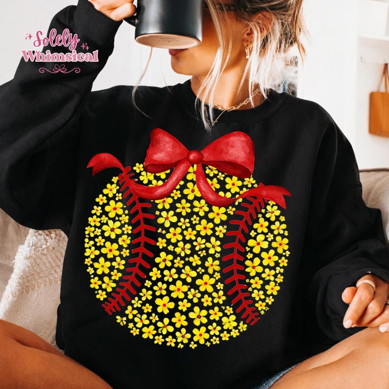 May include: Black sweatshirt featuring a baseball design made of yellow flowers and red stitching. A large red bow is at the top of the baseball. The text "Solely Whimsical" is in the upper left corner.