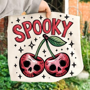 Może przedstawiać: Kremowa torba typu tote z upiornym wzorem. Słowo "SPOOKY" w czerwonych, obrysowanych literach znajduje się nad dwiema wiśniami z twarzami czaszek. Zielone łodygi i liście łączą wiśnie. Czarne gwiazdki otaczają wz&oacute;r.
