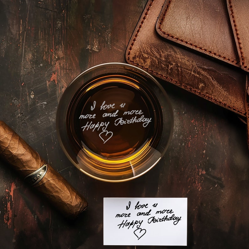 Puede incluir: Un vaso de l&iacute;quido &aacute;mbar con las palabras "I love u more and more Happy Birthday" escritas en el interior del vaso. Tambi&eacute;n se ve una cartera de cuero marr&oacute;n y un cigarro marr&oacute;n en la imagen.