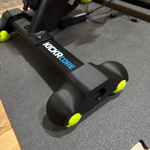 Könnte beinhalten: Schwarzes Trainingsgerät mit dem Text "KICKR CORE" in Weiß und Blau. Das Gerät hat gelbe Akzente und ist auf einer grauen Matte positioniert. Das Bild ist eine Nahaufnahme des Geräts.
