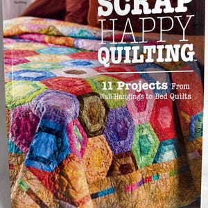 May include: A book cover titled "Scrap Happy Quilting" featuring a colorful quilt with a geometric pattern. The cover also includes the text "11 Projects From Wall Hangings to Bed Quilts" and the Annie's Quilting logo.