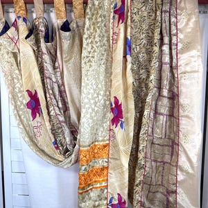 May include: A curtain panel featuring a patchwork of cream, gold, and tan fabric strips with magenta floral patterns, geometric shapes, and orange bands. The curtain hangs from a rod with gold fabric tabs and a visible measuring tape at the top.