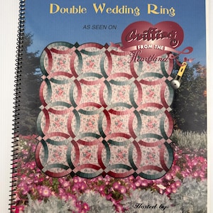 May include: A spiral-bound instructional book titled Double Wedding Ring, As Seen On Quilting From The Heartland, Hosted by Sharlene Jorgenson. The cover features a quilt with a floral pattern and interlocking rings in shades of red and green.