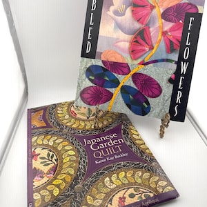 May include: Two instructional books on quilting. The top book is titled Fabled Flowers by Kumiko Sudo, featuring colorful fabric flower illustrations. The bottom book is titled Japanese Garden Quilt by Karen Kay Buckley, displaying circular quilt patterns with intricate leaf and floral designs in shades of purple, gold, and green.