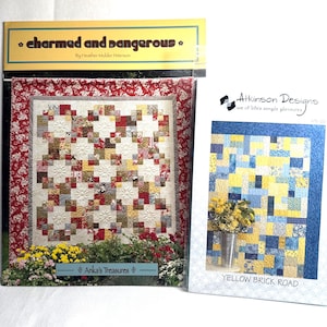 May include: Two quilt pattern books. The first book, "Charmed and Dangerous" by Heather Mulder Peterson, features a red and white quilt design. The second book, "Yellow Brick Road" by Atkinson Designs, showcases a yellow and blue quilt.