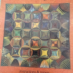 May include: A quilt pattern titled "Indian Orange Peel" with a repeating circular design in shades of orange, green, brown, and yellow. The pattern includes instructions and papers to complete a quilt measuring 63 inches by 63 inches.