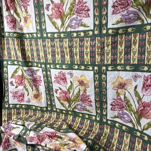 May include: A fabric textile featuring a repeating grid pattern of white squares containing illustrations of pink, purple, and yellow tulips with butterflies. The squares are separated by dark green borders with small tulip and butterfly motifs.