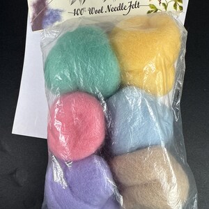 May include: A clear plastic bag containing six distinct balls of wool roving in mint green, yellow, pink, light blue, lavender, and beige. The header card reads National Nonwovens Wool Wisps 100% Wool Needle Felt with a floral graphic illustration.