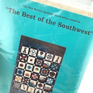 May include: A teal paper cover titled The New Mexico Quilters' Association presents The Best of the Southwest. It features a grid-patterned quilt illustration with various small square blocks depicting desert-themed icons and geometric shapes.