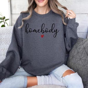 May include: A dark grey sweatshirt with the text "homebody" in black script with a small red heart underneath.