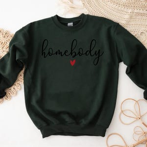 May include: A dark green sweatshirt with the text "homebody" in black cursive lettering and a small red heart.