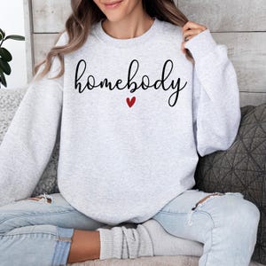 May include: A grey sweatshirt with the text "homebody" in black cursive lettering and a small red heart.