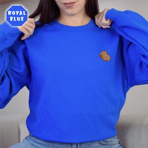 May include: A royal blue sweatshirt with a small embroidered brown capybara on the left chest.