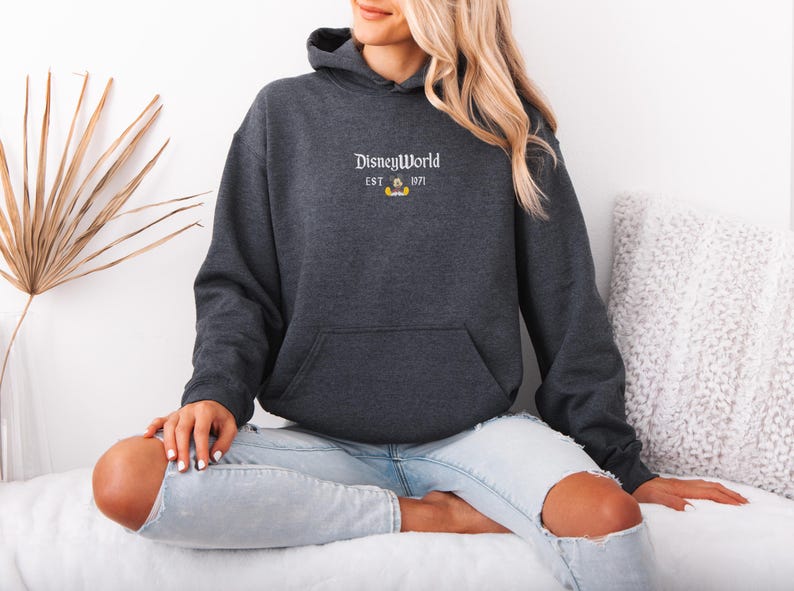 May include: Charcoal gray hoodie with a front pocket and a hood. The hoodie features the text "DisneyWorld EST. 1971" in white, with a small Mickey Mouse graphic. The sweatshirt is a casual style.
