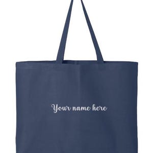 May include: A navy blue tote bag with long handles. The bag features the text "Your name here" in a cursive font. The bag is made of a sturdy material and is designed for carrying items.