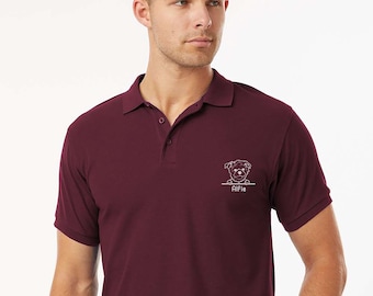 May include: Maroon polo shirt with a white embroidered dog graphic and the name "Alfie" below it. The shirt has a collared neckline and short sleeves. The model is wearing a black belt.