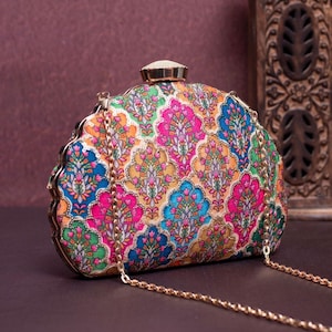 May include: A colorful, patterned clutch with a gold chain strap. The clutch features a repeating floral design in shades of pink, blue, orange, and green. The clasp is a small, gold-toned rectangle. The bag is a stylish accessory.