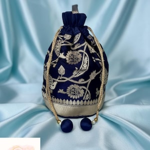 May include: Navy blue drawstring bag with gold floral embroidery. The bag features a gold drawstring cord and two navy blue tassel accents. The bag is sitting on a light blue satin surface. The bag is a stylish accessory.