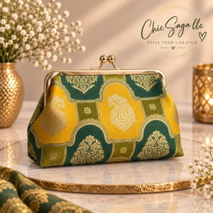 May include: A rectangular clutch purse featuring a gold-tone metal kiss-lock frame. The fabric displays a repeating pattern of yellow and dark green panels with intricate gold paisley and floral motifs. The purse has a structured, boxy shape.