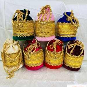 May include: A collection of seven velvet drawstring bags in various colors, including green, pink, blue, cream, red, and burgundy. Each bag is adorned with gold-colored trim and a beaded drawstring. The bags measure 13 cm x 21 cm.